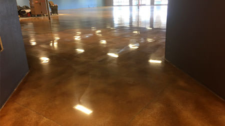 Interior view of a spacious room with polished concrete flooring reflecting numerous square patches of sunlight, possibly from a large window out of frame.