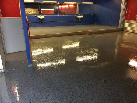 Reflective speckled flooring in an industrial or commercial space with blue and red walls, and a partially visible 'Lucky's' sign above a white sink. Bright overhead lights create a gleaming effect on the floor, enhancing the visibility of the room's features and the contrasting colors.