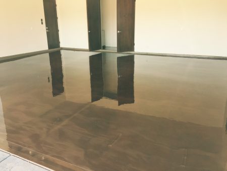 Inside a room with a highly reflective, polished brown floor, the sheen is so pronounced that it mirrors the wooden doors and white walls of the space. The room is well-lit, with no furniture, suggesting a clean, open, and versatile area within a commercial or residential setting. The clear reflections on the floor give the space a sense of depth and openness.