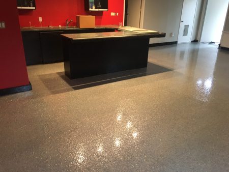 A commercial space featuring a sparkling grey epoxy floor that reflects the room’s lighting. Red walls and a large black counter with a glossy top enhance the modern aesthetic. The area appears clean and well-maintained, ready for use. The room's lighting and reflective floor create a bright and inviting atmosphere, suitable for a retail or hospitality setting.