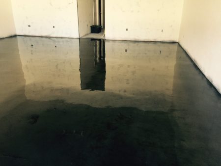 mpty commercial space with a reflective epoxy-coated floor showing signs of recent cleaning or finishing, with white walls featuring electrical outlets and a small trash bin in the corner, awaiting further development or occupancy.