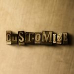 The word 'CUSTOMIZE' spelled out in vintage metal letterpress printing blocks, centered and casting a shadow on a textured beige background.