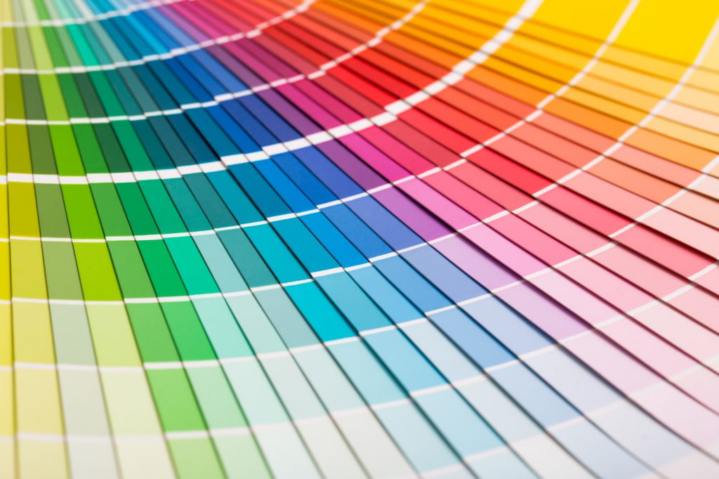 A close-up photo of a color spectrum displayed on a fan deck with a range of hues from vibrant greens, blues, and purples to warm reds, oranges, and yellows. The color swatches are neatly arranged in a semi-circular pattern, showcasing a gradient of shades used for color matching in design and painting projects.