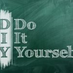 The acronym 'DIY' which stands for 'Do It Yourself,' is written in large white chalk letters on a dark green chalkboard. The first letters of each word are vertically aligned to form the acronym 'DIY' with the rest of the words written to the right, creating an instructional or motivational message often associated with crafting or home improvement projects.