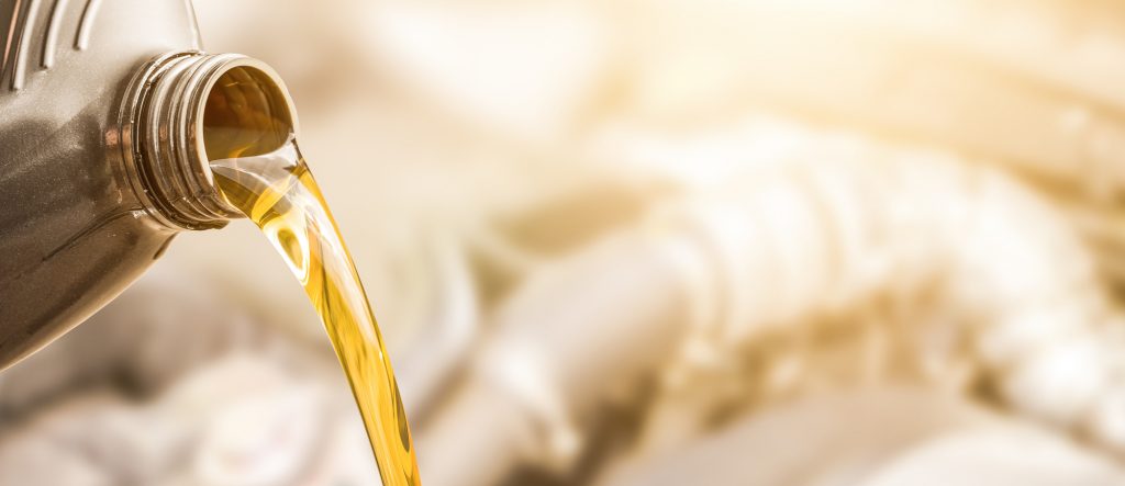 Golden motor oil pouring from a plastic container against a blurred background, showcasing the viscosity and smooth flow of the lubricant with a warm color tone that emphasizes its texture and use in machinery maintenance.