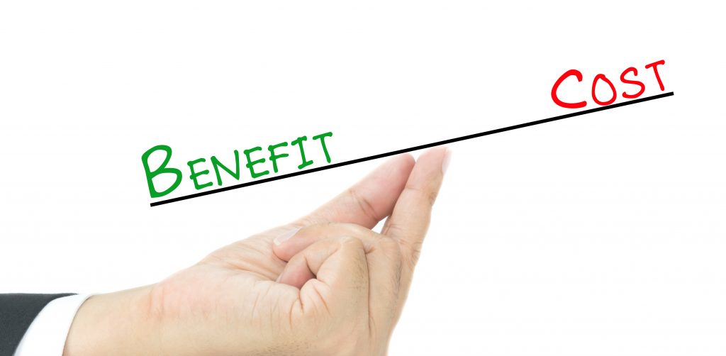 A hand balancing an imaginary scale with the words 'BENEFIT' in green on the lower side and 'COST' in red on the higher side, against a white background. The hand is tipping towards 'BENEFIT', symbolizing a weighing of pros and cons where benefits outweigh costs.