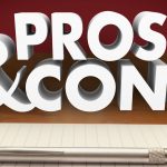 The words 'PROS & CONS' in large, bold, 3D letters appear to float above a notebook and a pen on a wooden surface. The background has a warm, dark red tone that contrasts with the white text, emphasizing the theme of weighing different sides of an argument or decision.