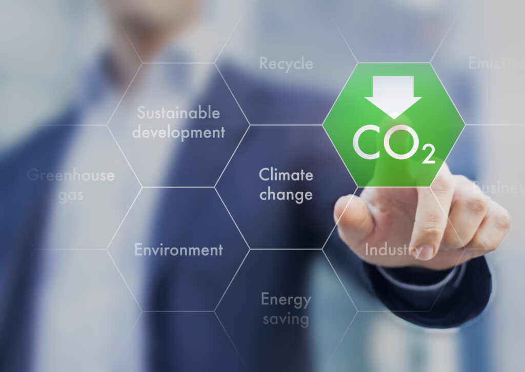 A person in a business suit interacting with a digital interface, focusing on a hexagonal button labeled 'CO2' with a downward arrow, surrounded by concepts like 'Climate change', 'Energy saving', and 'Sustainable development'.
