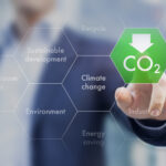 A person in a business suit interacting with a digital interface, focusing on a hexagonal button labeled 'CO2' with a downward arrow, surrounded by concepts like 'Climate change', 'Energy saving', and 'Sustainable development'.