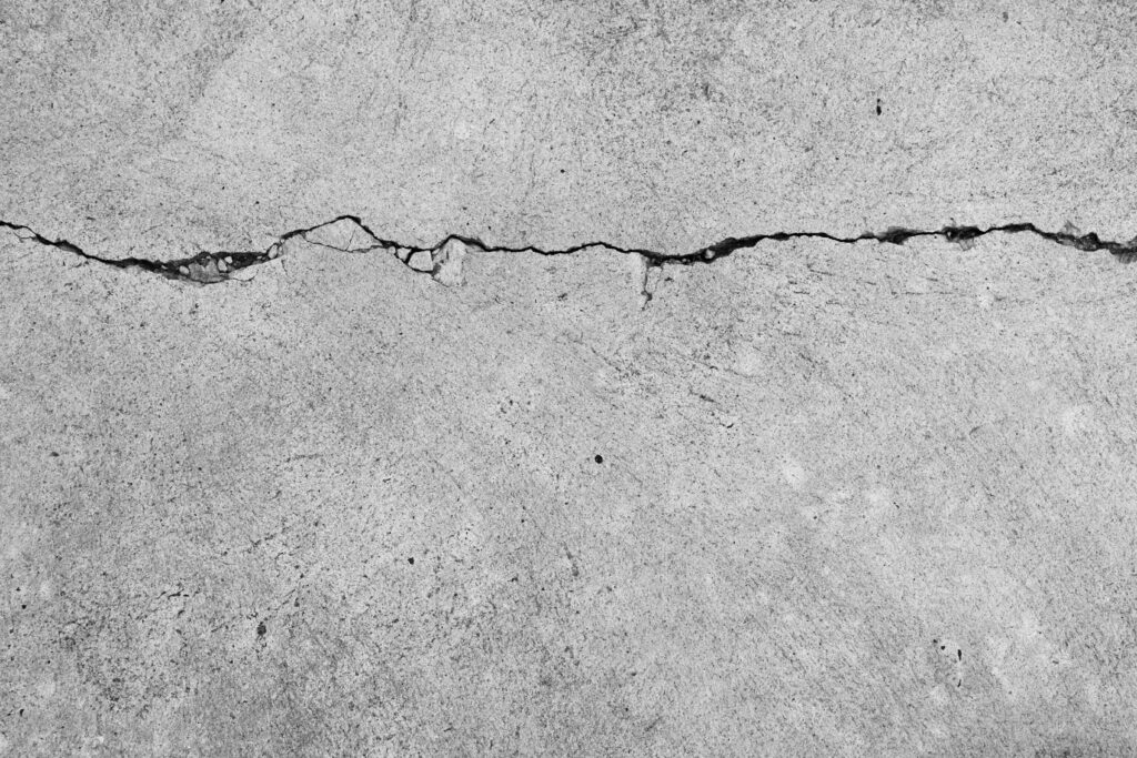 Close-up of a jagged crack running through a concrete surface, depicting the texture and irregular pattern of the break.