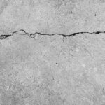 Close-up of a jagged crack running through a concrete surface, depicting the texture and irregular pattern of the break.