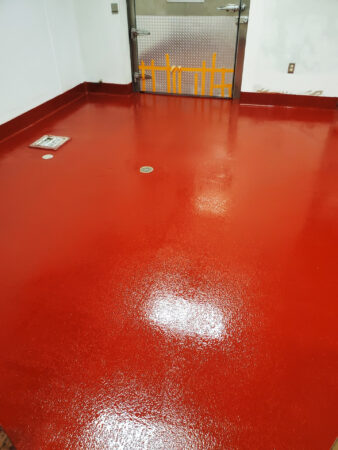 A room with glossy red epoxy flooring reflecting overhead lighting, featuring clean white walls with multiple water outlets, possibly in a commercial or industrial setting.