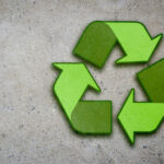 A vibrant green recycling symbol composed of three chasing arrows on a rough concrete surface, representing the concept of sustainability and environmental conservation.