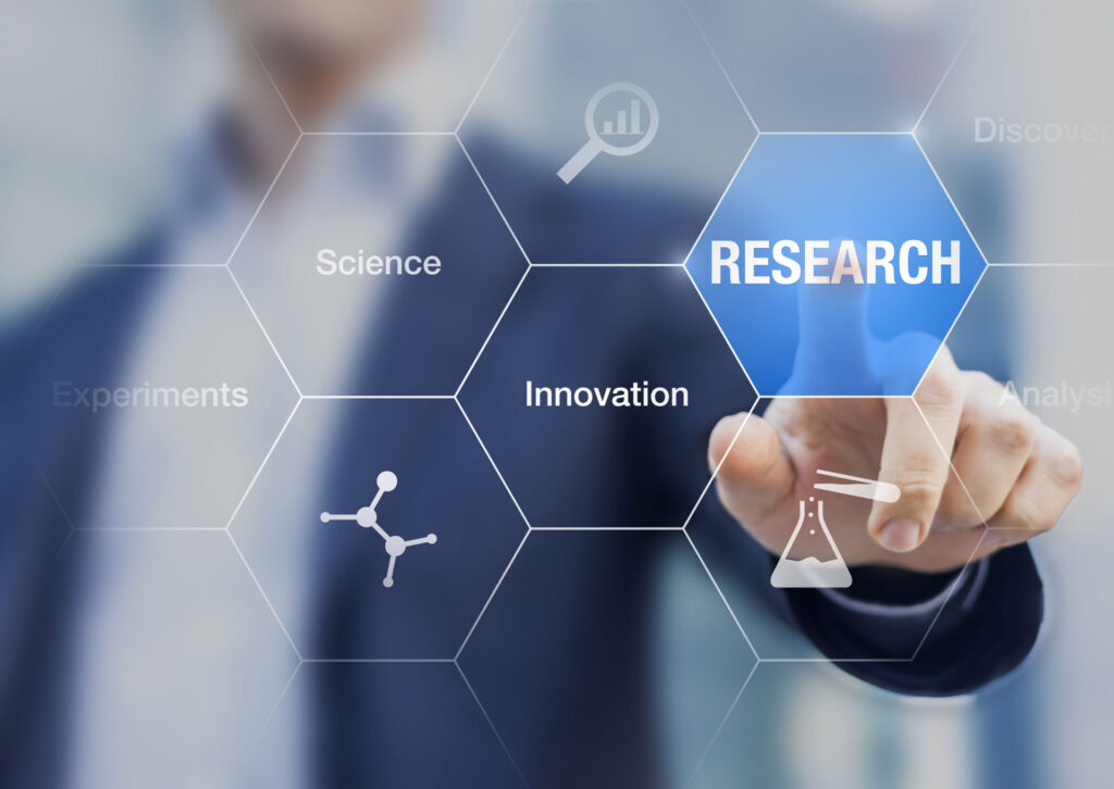 Business professional interacting with a futuristic holographic interface with the word 'RESEARCH' highlighted in blue. Surrounding keywords like 'Science', 'Innovation', and 'Experiments' are connected in a hexagonal pattern, suggesting a theme of scientific discovery and analysis.