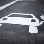 Painted symbol on concrete asphalt depicting an electric vehicle with a plug, indicating a parking space designated for charging electric cars.