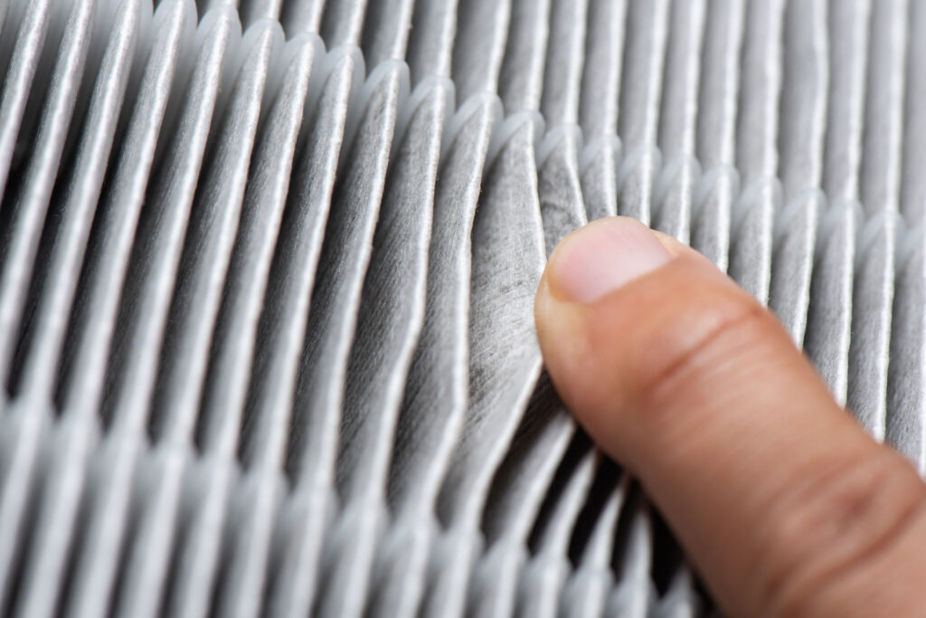 Close-up image of a human finger pressing against a pleated air filter, highlighting the texture and layers of the filtration material.