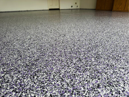 Garage with newly resurfaced epoxy concrete coating. The epoxy flooring is flecked with purple and black.