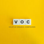 A minimalistic image with the letters 'VOC' displayed on three white square tiles against a bright yellow background. Below the tiles, the text 'Volatile Organic Compounds' is written in black, centered beneath the letters.