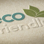 Embossed 'eco-friendly' design on textured beige paper. The word 'eco' is in greenish-blue, while 'friendly' is embossed in a subtle, raised style. A green leaf illustration extends from the letter 'o,' emphasizing the sustainability theme.