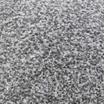 Close-up of a rough-textured surface with a speckled pattern of small, irregular black, gray, and white flakes, resembling a pebble dash or terrazzo floor finish.
