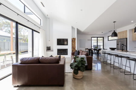 Bright open-plan living area with polished concrete floors, brown leather sofas, and modern kitchen with island seating.