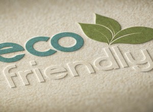 Embossed 'eco-friendly' design on textured beige paper. The word 'eco' is in greenish-blue, while 'friendly' is embossed in a subtle, raised style. A green leaf illustration extends from the letter 'o,' emphasizing the sustainability theme.