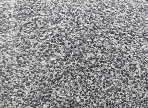 Close-up of a rough-textured surface with a speckled pattern of small, irregular black, gray, and white flakes, resembling a pebble dash or terrazzo floor finish.