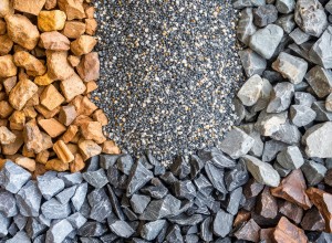 A top-down view of four different types of rocks and gravel, neatly arranged in sections. Clockwise from the top left: coarse orange-brown rocks, small multicolored gravel, grayish-white rocks, and dark brown rocks with a polished appearance. Each type of material contrasts in texture and color, showcasing their distinct characteristics.