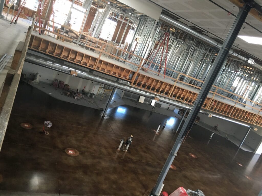 A large room with a high-shine marbled brown concrete floor, showing reflections of ceiling lights and colored walls, with a fire extinguisher mounted on a column, giving the space a functional yet polished appearance.