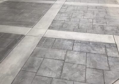 Elegant outdoor patio area with gray stamped concrete tiles arranged in a pattern, leading to a classic white balustrade and a stone bench set, suggesting a sophisticated and tranquil outdoor living space.