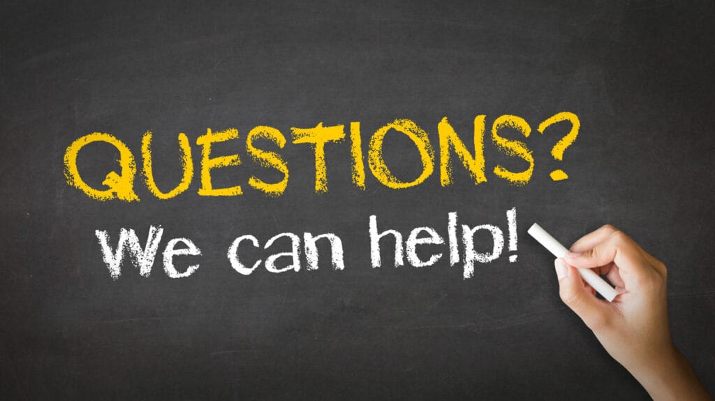 A person's hand holding white chalk against a blackboard with the words 'QUESTIONS? We can help!' written in bold, yellow chalk. The text on the blackboard is clear and stands out, suggesting an offer of assistance to decide between polyaspartic and epoxy topcoats for concrete floors.