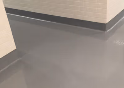 A newly finished floor with glossy epoxy coating reflecting the light, complementing the white tiled walls with a dark baseboard. The image showcases a clean and sleek commercial or industrial space, emphasizing the floor's smooth and shiny surface.