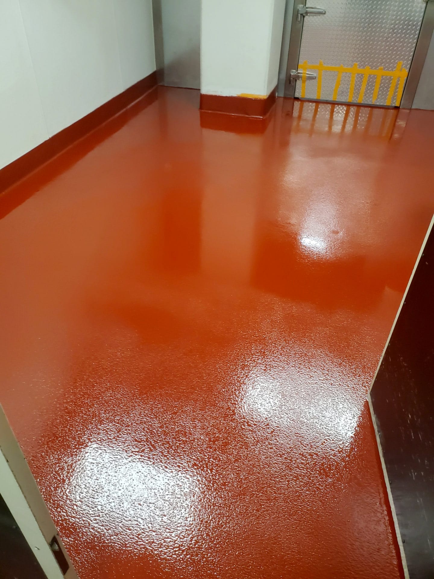 A room with glossy red epoxy flooring reflecting overhead lighting, featuring clean white walls with multiple water outlets, possibly in a commercial or industrial setting.