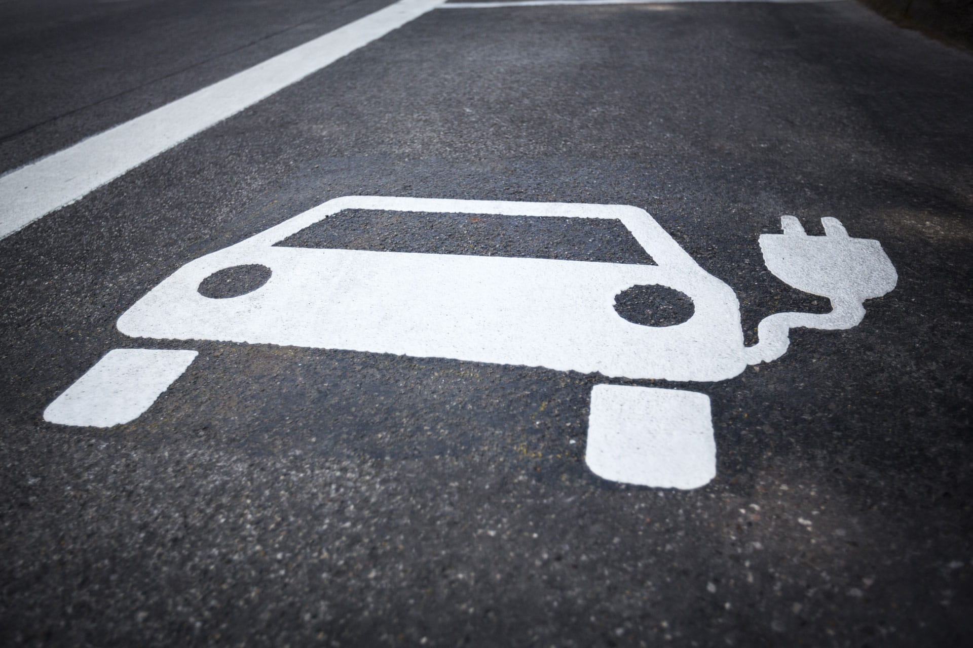 Painted symbol on concrete asphalt depicting an electric vehicle with a plug, indicating a parking space designated for charging electric cars.