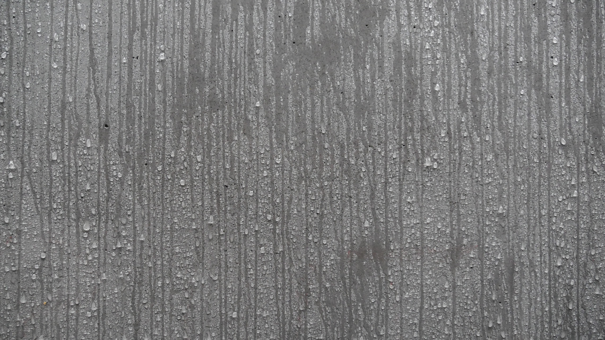 Close-up of vertical streaks and water droplets on a concrete, showing moisture on the material.